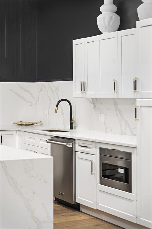 kitchen with white cabinets, light hardwood / wood-style floors, stainless steel dishwasher, and sink