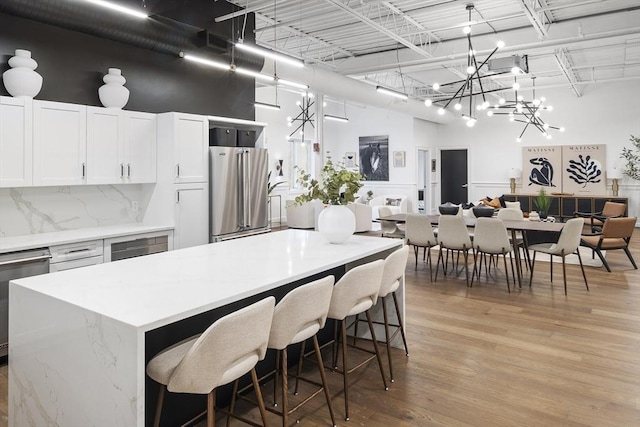 kitchen featuring white cabinetry, backsplash, light hardwood / wood-style floors, decorative light fixtures, and appliances with stainless steel finishes