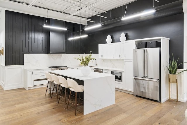 kitchen featuring appliances with stainless steel finishes, light wood-type flooring, a breakfast bar, white cabinets, and a kitchen island