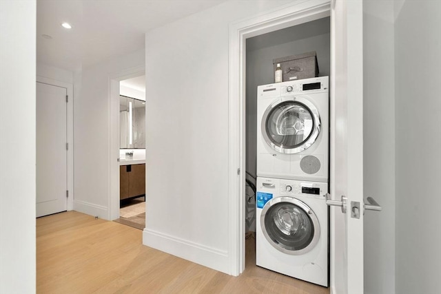 clothes washing area with light hardwood / wood-style floors and stacked washer and clothes dryer