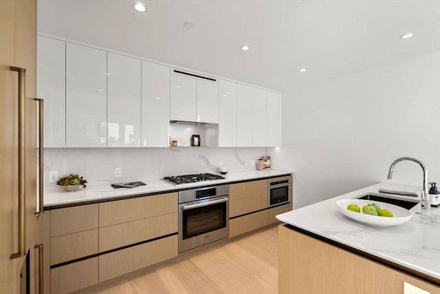 kitchen featuring light brown cabinetry, appliances with stainless steel finishes, tasteful backsplash, white cabinets, and light hardwood / wood-style flooring