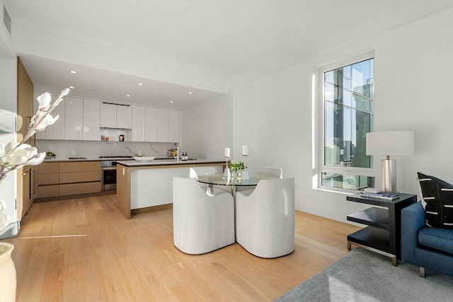 kitchen featuring a wealth of natural light, white cabinets, appliances with stainless steel finishes, a kitchen island with sink, and light wood-type flooring