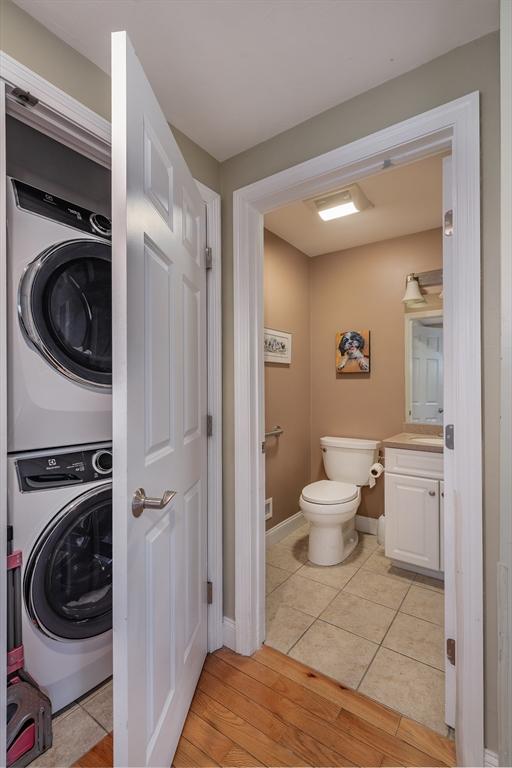 laundry area with stacked washer and clothes dryer, light wood finished floors, a sink, laundry area, and baseboards