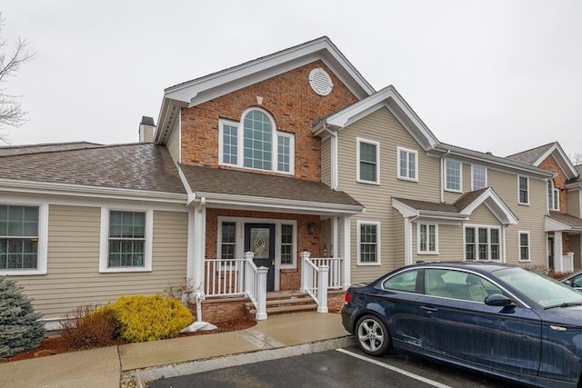 view of front of house featuring uncovered parking, brick siding, a chimney, and a shingled roof