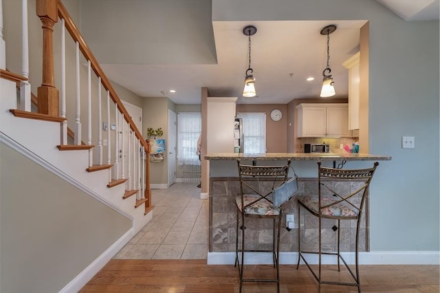 kitchen featuring baseboards, light wood-type flooring, decorative backsplash, stainless steel microwave, and pendant lighting