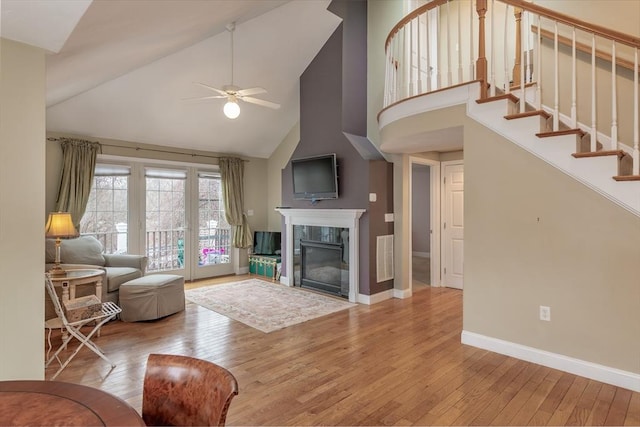 living room featuring hardwood / wood-style flooring, ceiling fan, stairs, a fireplace, and high vaulted ceiling