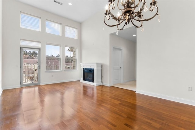 unfurnished living room featuring wood-type flooring, a premium fireplace, a towering ceiling, and a chandelier