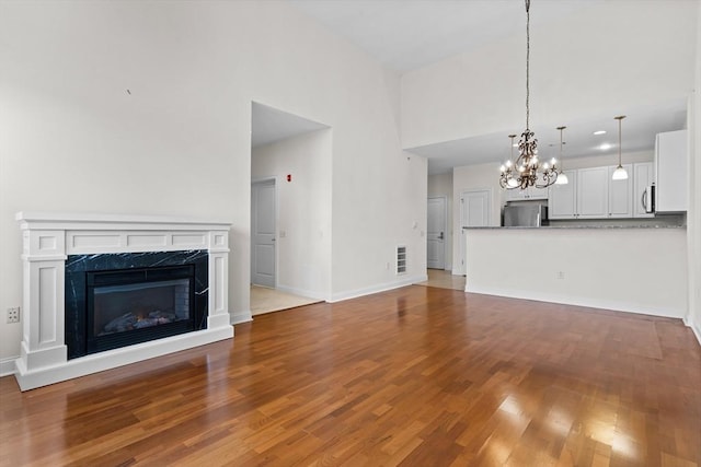 unfurnished living room featuring a fireplace, a towering ceiling, light wood-type flooring, and a notable chandelier