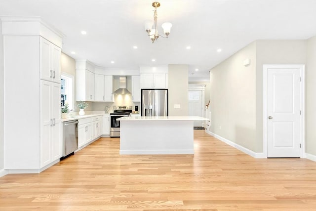 kitchen with light wood-style flooring, wall chimney exhaust hood, white cabinets, and appliances with stainless steel finishes