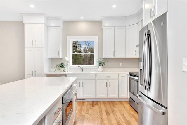 kitchen featuring recessed lighting, light wood-style flooring, appliances with stainless steel finishes, white cabinetry, and a sink