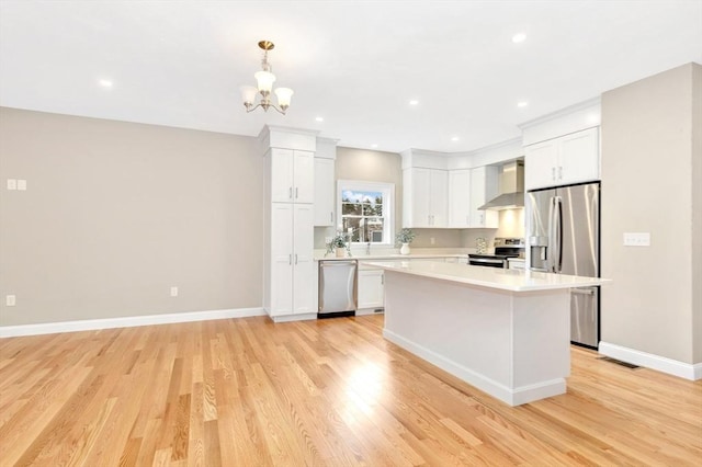 kitchen with light wood finished floors, light countertops, appliances with stainless steel finishes, white cabinets, and wall chimney exhaust hood