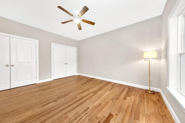 unfurnished bedroom featuring baseboards, light wood-type flooring, multiple closets, and a ceiling fan