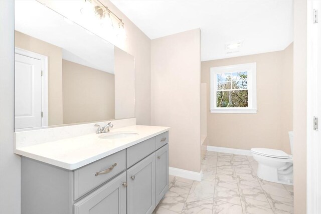 bathroom with vanity, toilet, baseboards, and marble finish floor