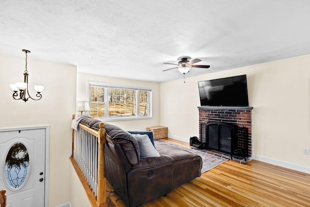 living room with wood-type flooring, ceiling fan with notable chandelier, and a fireplace