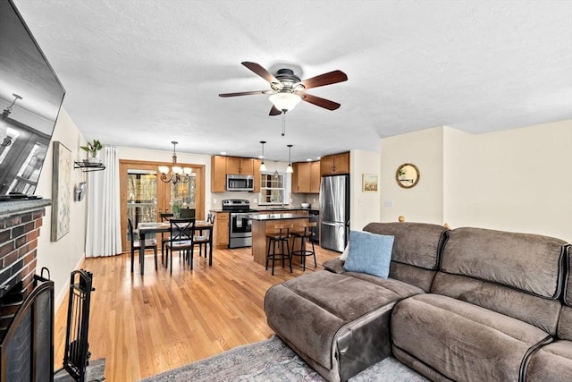 living room featuring a textured ceiling, light hardwood / wood-style floors, ceiling fan with notable chandelier, and a brick fireplace