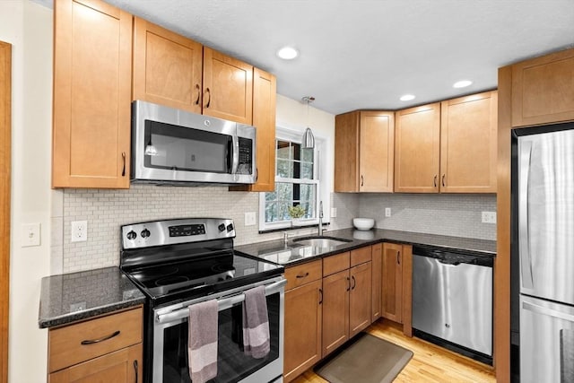 kitchen featuring pendant lighting, appliances with stainless steel finishes, sink, light wood-type flooring, and dark stone countertops