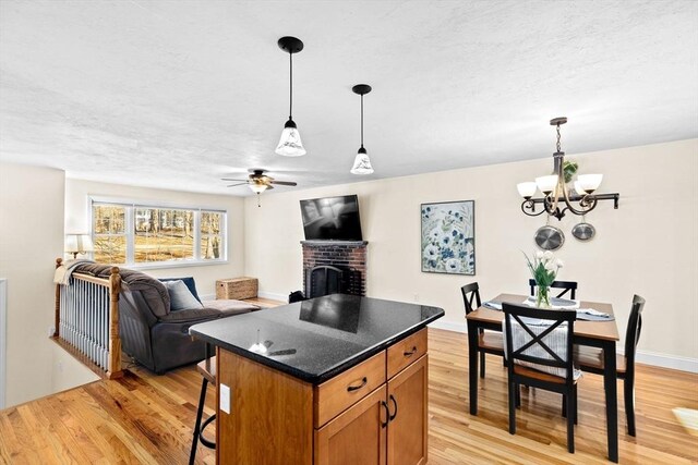 kitchen with a kitchen island, a brick fireplace, light hardwood / wood-style flooring, and pendant lighting