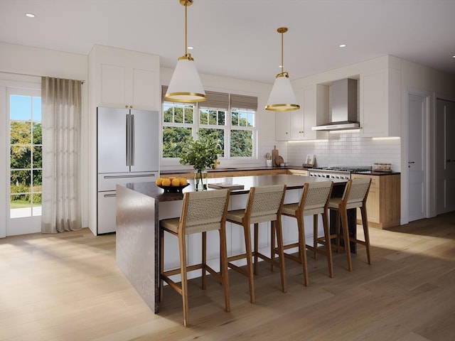 kitchen with white cabinetry, high end refrigerator, decorative light fixtures, a kitchen island, and wall chimney range hood