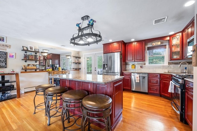 kitchen featuring appliances with stainless steel finishes, reddish brown cabinets, light wood-type flooring, plenty of natural light, and recessed lighting