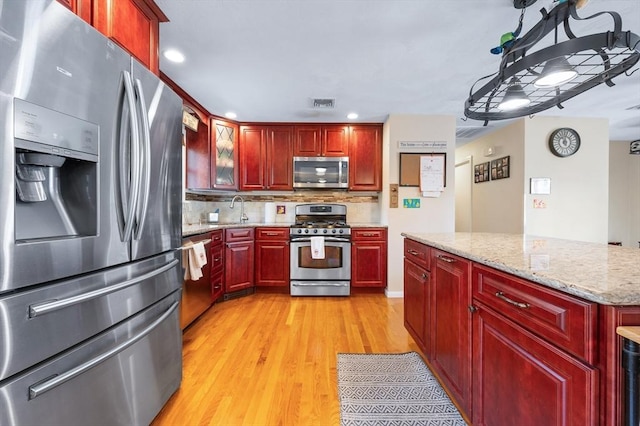 kitchen featuring appliances with stainless steel finishes, reddish brown cabinets, light wood-style floors, tasteful backsplash, and light stone counters
