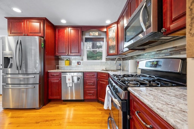 kitchen with appliances with stainless steel finishes, dark brown cabinets, recessed lighting, a sink, and light stone counters