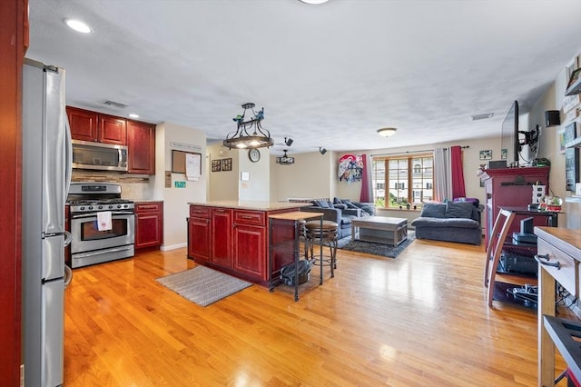 kitchen featuring appliances with stainless steel finishes, reddish brown cabinets, open floor plan, light wood finished floors, and recessed lighting