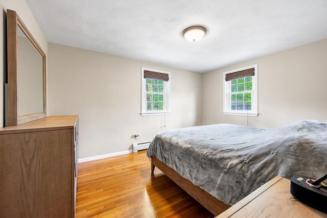 bedroom with a baseboard heating unit, multiple windows, light wood finished floors, and baseboards