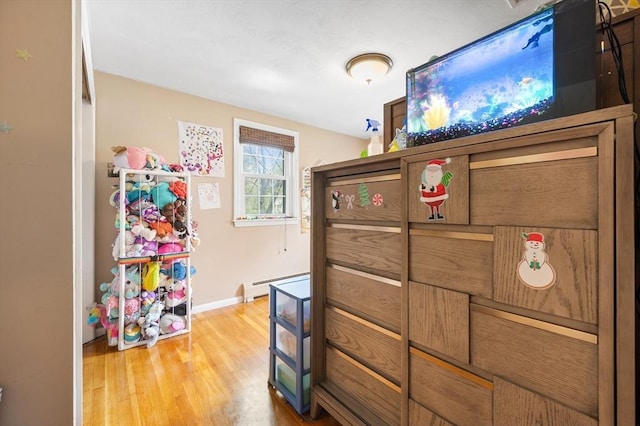 bedroom with a baseboard radiator, light wood finished floors, and baseboards