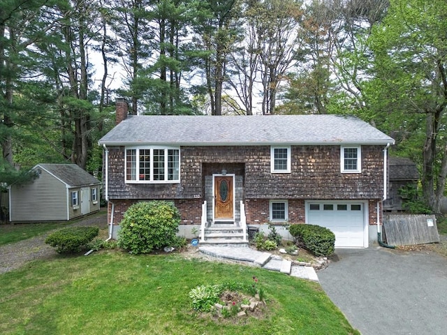 raised ranch featuring asphalt driveway, a garage, a chimney, and a front yard