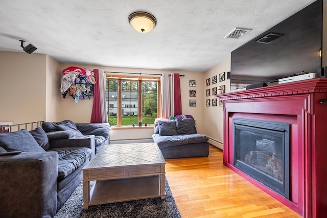living area with wood finished floors, a glass covered fireplace, and baseboard heating