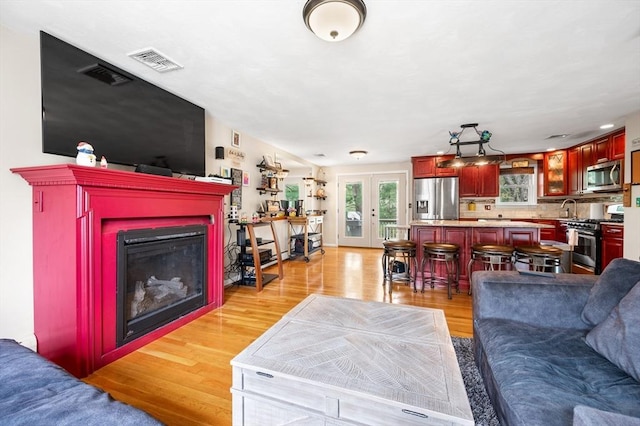 living area with healthy amount of natural light, light wood finished floors, a fireplace, and french doors