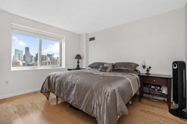 bedroom featuring a view of city, baseboards, wood finished floors, and visible vents