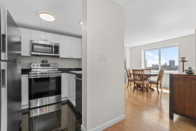 kitchen featuring decorative backsplash, dark countertops, baseboards, white cabinets, and appliances with stainless steel finishes