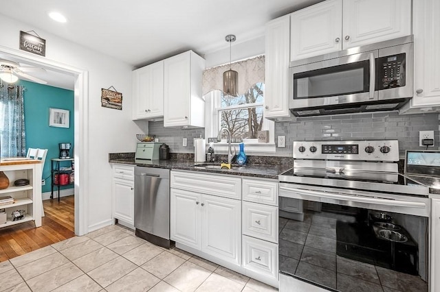 kitchen with light tile patterned flooring, sink, white cabinetry, hanging light fixtures, and stainless steel appliances