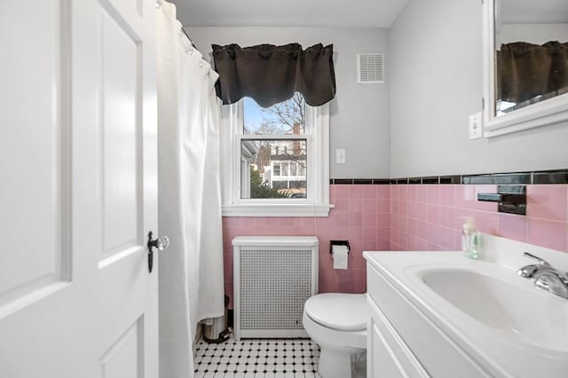 bathroom with tile walls, toilet, vanity, and radiator