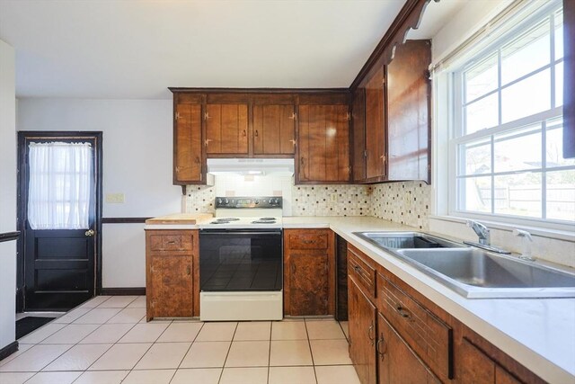kitchen with a sink, light countertops, under cabinet range hood, and electric range