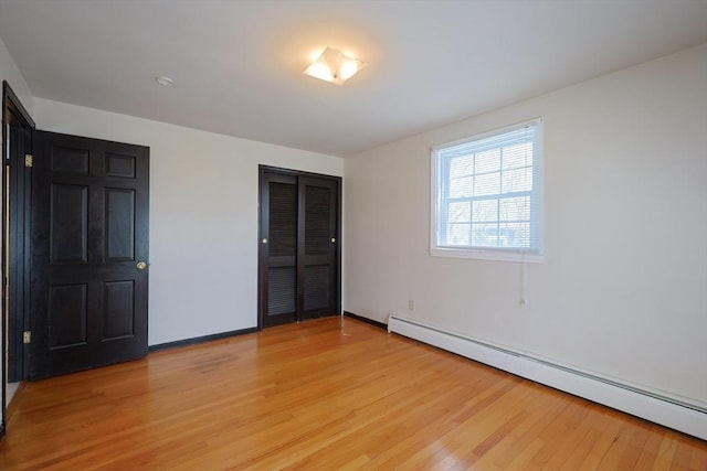 unfurnished bedroom with a closet, baseboards, a baseboard heating unit, and light wood-type flooring