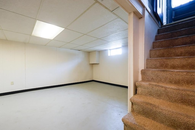 basement featuring baseboards, stairs, and a paneled ceiling