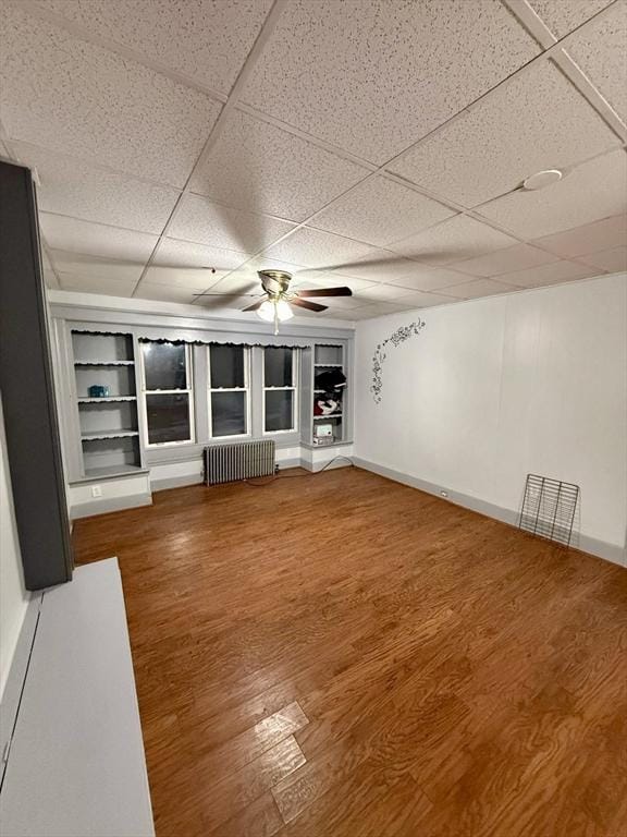 unfurnished living room featuring a paneled ceiling, ceiling fan, hardwood / wood-style floors, and radiator heating unit