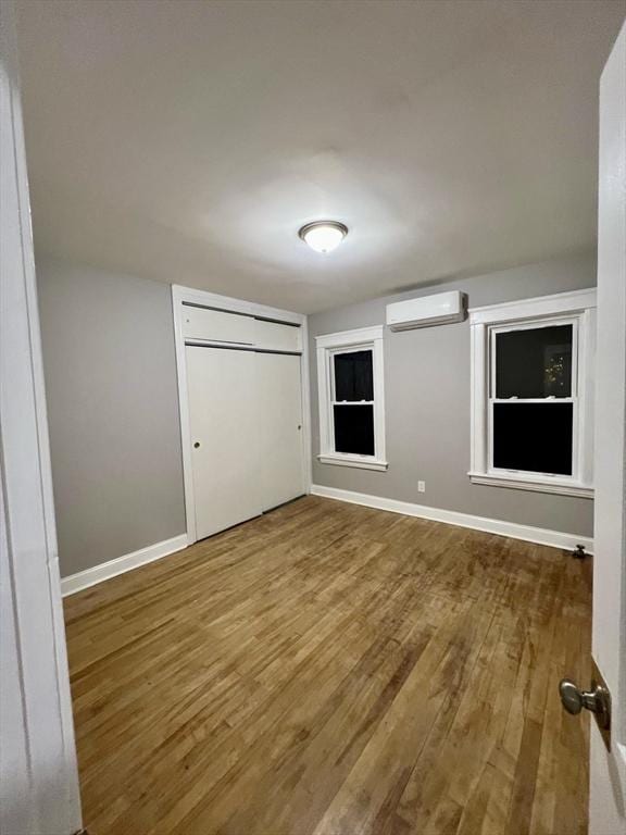 unfurnished bedroom featuring a closet, hardwood / wood-style flooring, and a wall mounted air conditioner