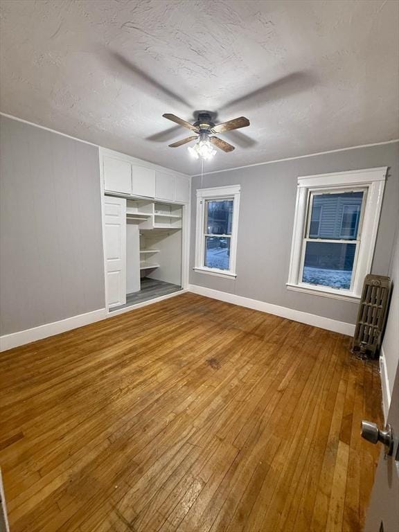 unfurnished bedroom with ceiling fan, radiator heating unit, wood-type flooring, and a closet