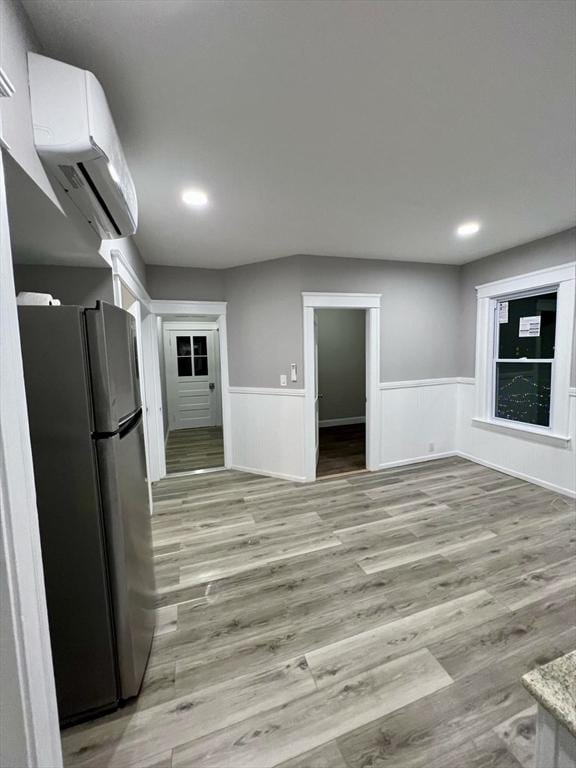 kitchen featuring a wall mounted AC, stainless steel refrigerator, white cabinetry, and light hardwood / wood-style flooring