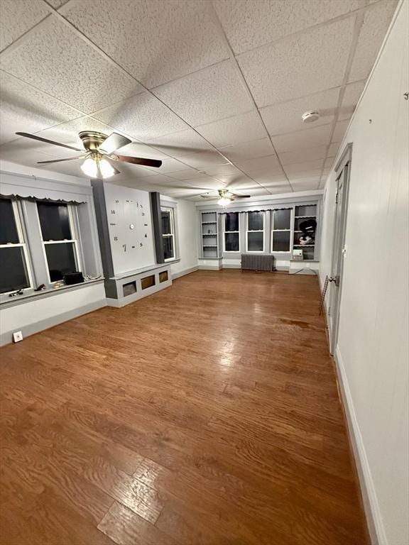 unfurnished living room with a drop ceiling, hardwood / wood-style floors, radiator heating unit, and built in shelves