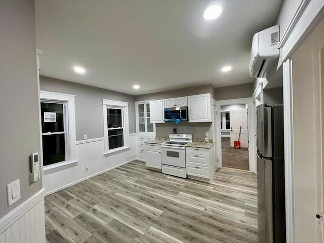 kitchen featuring white cabinetry, a wall unit AC, stainless steel appliances, light wood-type flooring, and light stone countertops