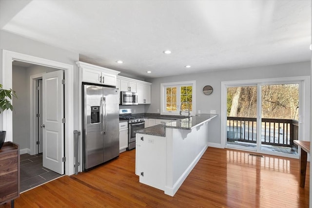 kitchen featuring a breakfast bar, dark wood finished floors, stainless steel appliances, white cabinetry, and a peninsula