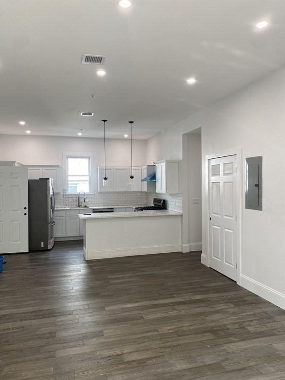 kitchen with white cabinets, wall chimney range hood, stainless steel fridge, decorative light fixtures, and dark hardwood / wood-style flooring