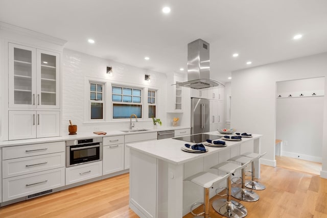 kitchen featuring island exhaust hood, stainless steel appliances, a kitchen island, sink, and light hardwood / wood-style floors