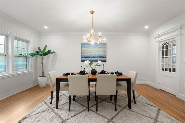 dining space with light wood-type flooring, crown molding, and an inviting chandelier