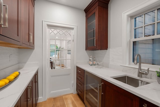 bar with light stone countertops, sink, light wood-type flooring, and tasteful backsplash