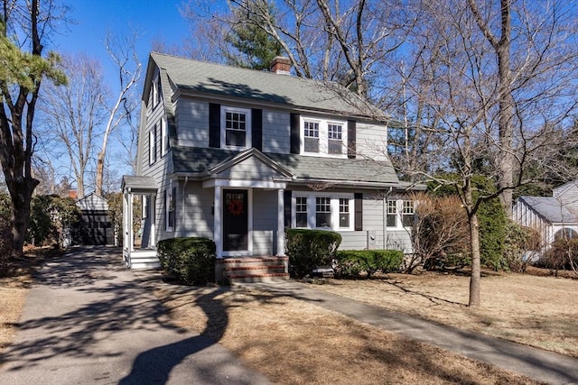 view of front facade with a chimney, a gambrel roof, driveway, and a shingled roof